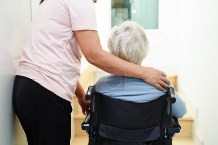 Asian senior woman on wheelchair with caregiver help support walking down the stairs prevent accident, slip and fall at home.
