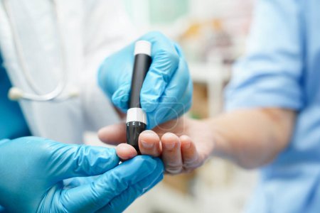 Téléchargez les photos : Médecin asiatique utilisant un stylo lancette sur le doigt du patient âgé pour vérifier le taux de sucre dans le sang de l'échantillon pour le traitement du diabète. - en image libre de droit