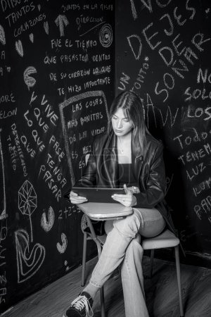 Foto de Imagen en blanco y negro de una hermosa joven sentada en una silla de la universidad con un ordenador portátil - Imagen libre de derechos