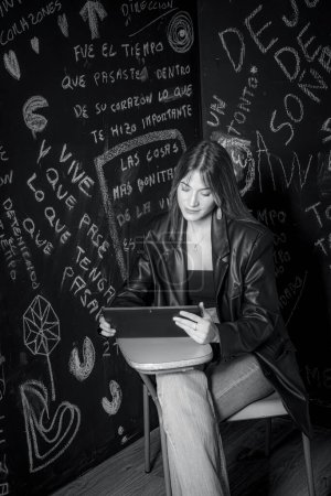 Foto de Imagen en blanco y negro de una hermosa joven sentada en una silla de la universidad con un ordenador portátil - Imagen libre de derechos
