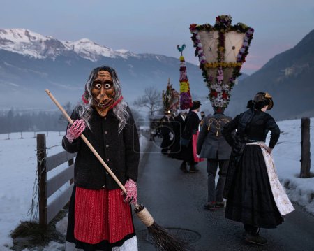 Foto de AUSTRIA, GASTEIN - January 1, 2023: Witch with a broom and dancing perchten against the backdrop of mountains. High quality photo - Imagen libre de derechos