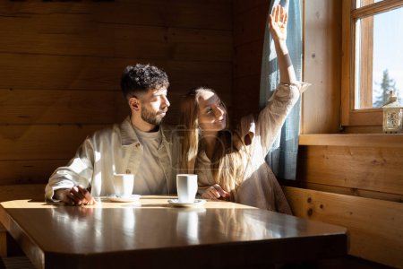 Téléchargez les photos : Jeune couple assis dans un café près d'une fenêtre avec un soleil éclatant. Photo de haute qualité - en image libre de droit