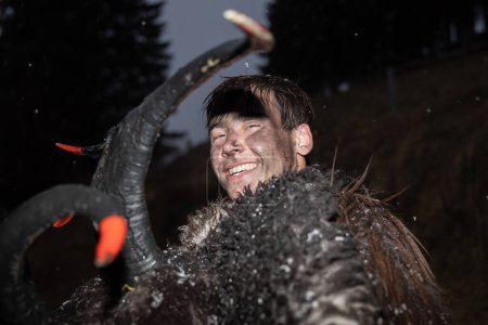 Téléchargez les photos : Portrait d'un jeune homme à l'image du légendaire krampus, héros des festivités de Noël, sur fond de forêt et de flocons de neige. Photo de haute qualité - en image libre de droit