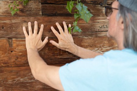 Téléchargez les photos : L'homme posa les mains sur les vieux murs en bois d'un immeuble résidentiel. Photo de haute qualité - en image libre de droit