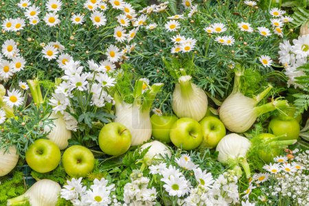 Foto de Varieties of seasonal fruits and vegetables set on a background of foliage with daisies. Green apples and fennel bulbs. - Imagen libre de derechos