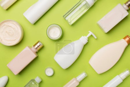 Different cosmetic bottles and container on color background, top view.