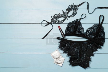 Lace mask, lingerie and condoms on wooden background, top view.