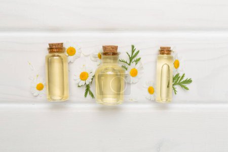 Foto de Botellas con aceite esencial de manzanilla y flores sobre fondo de madera, vista superior - Imagen libre de derechos