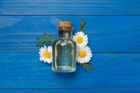 Foto de Botella con aceite esencial de manzanilla y flores sobre fondo de madera, vista superior - Imagen libre de derechos