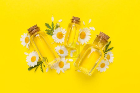 Foto de Botellas con aceite esencial de manzanilla y flores sobre fondo de color, vista superior - Imagen libre de derechos