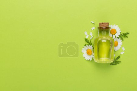 Foto de Botella con aceite esencial de manzanilla y flores sobre fondo de color, vista superior - Imagen libre de derechos