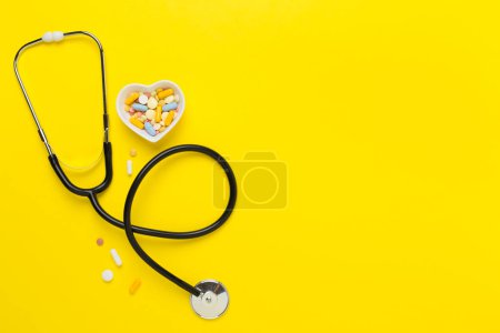 Stethoscope with heart medicines on color background, top view