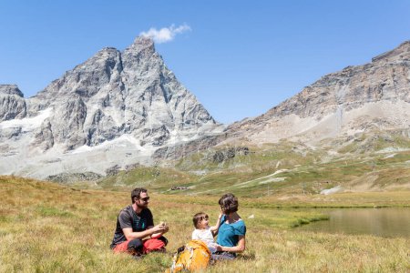 Téléchargez les photos : Couple avec sa petite fille qui pique-nique près d'un lac sous le Cervin dans les Alpes italiennes. - en image libre de droit
