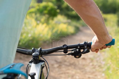 Foto de Vista trasera de un ciclista masculino sosteniendo una bicicleta de montaña antes de montarla en una pista de tierra provista de plantas verdes. - Imagen libre de derechos