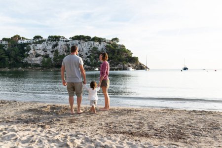 Foto de Familia feliz paseando por una bonita playa de arena llamada cala Galdana ubicada en Menorca, España. - Imagen libre de derechos