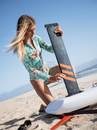 Foto de Blond caucasian female setting up hydrofoil surfing equipment on the beach - Imagen libre de derechos
