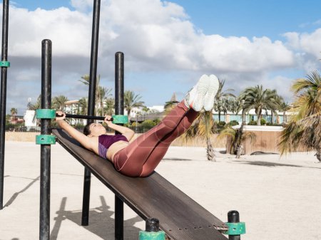 Foto de Young hispanic woman exercising abs outdoor at the calisthenics park - Imagen libre de derechos