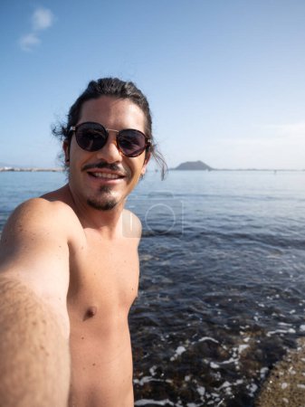 Photo for Hispanic man with long black hair and sunglasses selfie enjoying the summer by the sea - Royalty Free Image
