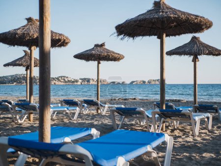 Téléchargez les photos : Plage de sable avec chaises longues bleues et parasols en paille et la mer en arrière-plan. Plage méditerranéenne Gran Tora à Paguera, Calvia - en image libre de droit