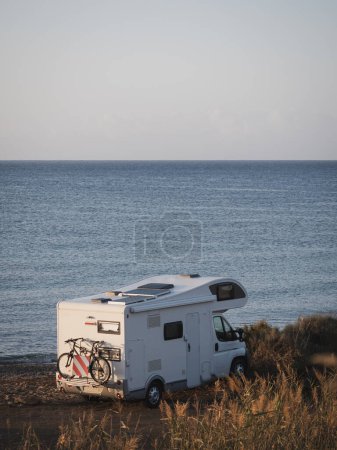 Foto de Autocaravana blanca estacionada en la playa al amanecer - Imagen libre de derechos