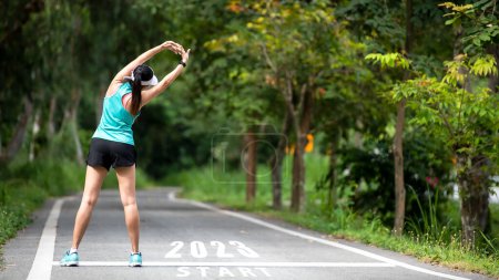 The start into the new year 2023. Start up of runner woman running on nature race track go to Goal of Success.  People running as part of Number 2023.  Holiday sport and health care Concept