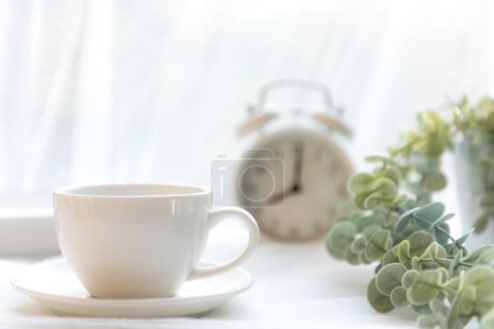 Select focus.  Coffee morning.  White steaming cup of hot coffee for relax after wake up, vintage alarm clock background. Lifestyle Concept