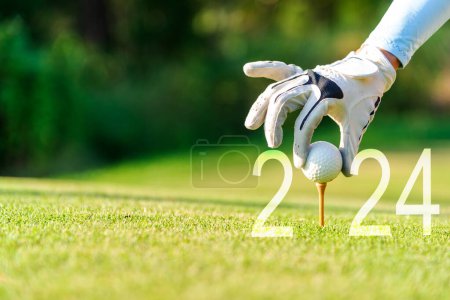 Close-up-Hand Golferin Golfball setzen für Happy New Year 2024 auf dem grünen Golf für neue gesunde. Kopierraum. Gesundes und Urlaubskonzept