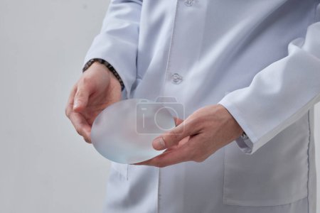 Téléchargez les photos : Implant mammaire en silicone dans la main d'un chirurgien plasticien, concept de mastopexie, LIFT - en image libre de droit