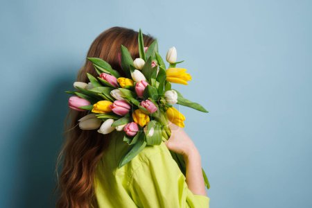 fille avec un bouquet de printemps de tulipes sur un fond bleu propre, fleurs de printemps