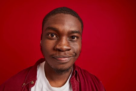 Close-up of a joyful young African American male with wireless headphones isolated on red background studio portrait