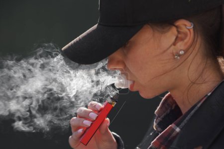 junges Mädchen raucht auf dunklem Hintergrund einen Vape in Großaufnahme, Frauen rauchen auf der Straße eine elektronische Zigarette
