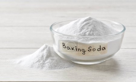 baking soda in a clear glass bowl on a light wooden table. Glass bowl of sodium bicarbonate on a white wooden table.