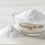 baking soda in a clear glass bowl on a light wooden table. Glass bowl of sodium bicarbonate on a white wooden table.