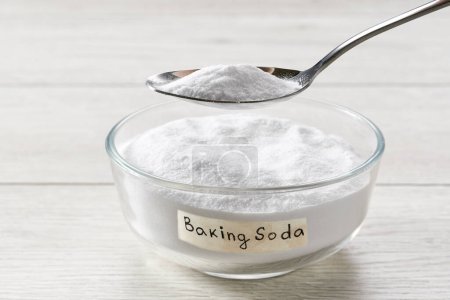 bowl with sodium bicarbonate on a whitet wooden table, plate with baking soda on wooden table.