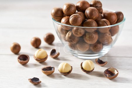 Photo for Macadamia in a clear glass bowl and scattered on a white kitchen table, selective focus. - Royalty Free Image