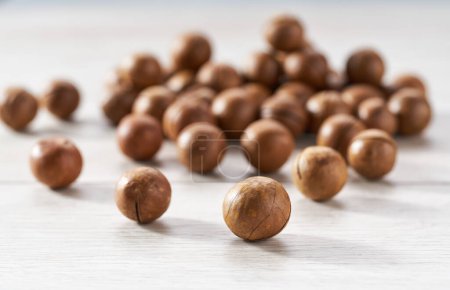 Téléchargez les photos : Tas ou pile de noix de macadamia sur une table de cuisine blanche, foyer sélectif. - en image libre de droit