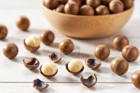 Photo for Macadamia spill out of a wooden plate on a white table. - Royalty Free Image