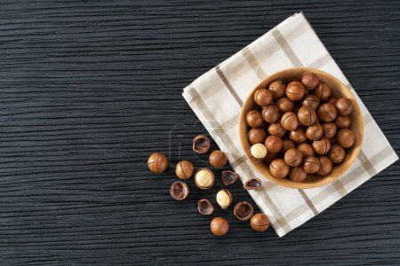 Foto de Placa de madera con nueces de macadamia sobre mesa negra. Espacio para texto - Imagen libre de derechos