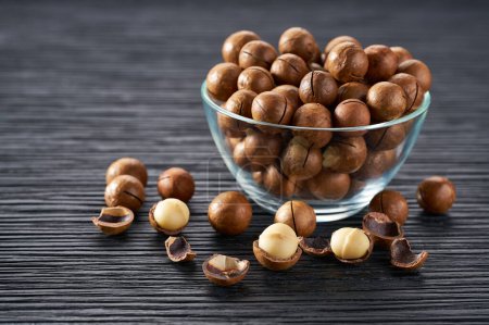 Photo for Macadamia in a clear glass bowl and scattered on a black table, selective focus. - Royalty Free Image