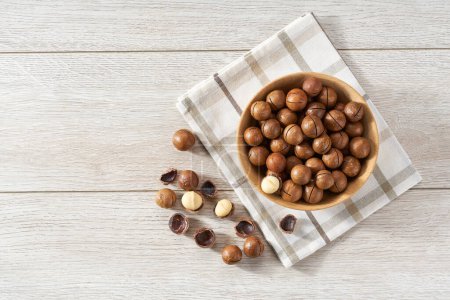 Photo for Wooden plate with macadamia nuts on white table. Space for text - Royalty Free Image