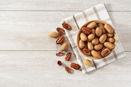 Photo for Wooden plate with pecan  nuts on white table. Space for text - Royalty Free Image