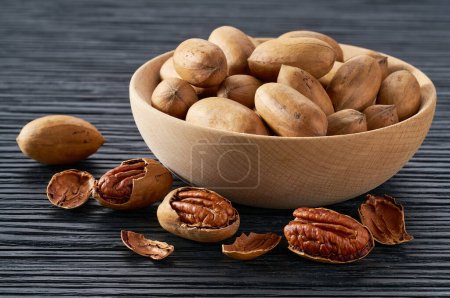 Photo for Wooden plate with organic pecan nuts on black table. - Royalty Free Image