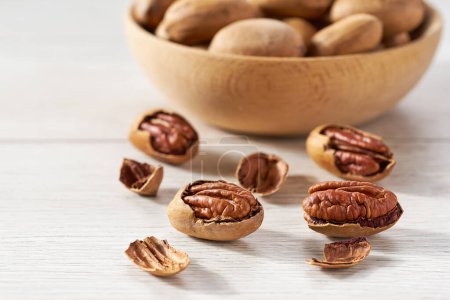 Photo for Pecan spill out of a wooden plate on a white table. - Royalty Free Image