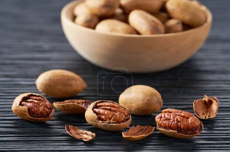 Photo for Pecan spill out of a wooden plate on a black table. - Royalty Free Image