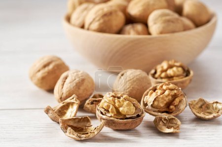 Photo for Walnuts spill out of a wooden plate on a white table. - Royalty Free Image