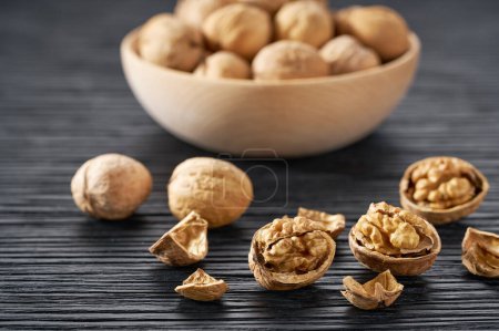 Photo for Walnuts spill out of a wooden plate on a black table. - Royalty Free Image