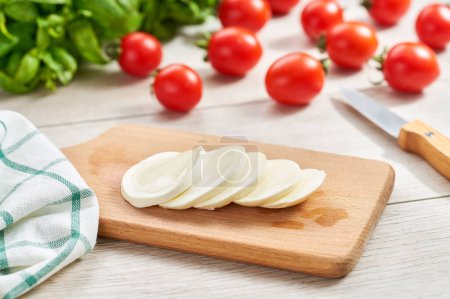 Foto de Bolas de queso mozzarella con tomate y albahaca en una mesa de cocina blanca, ingredientes para ensalada caprese. - Imagen libre de derechos