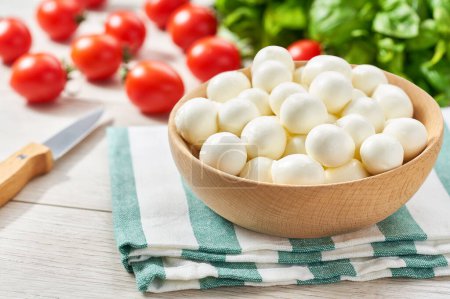 Photo for Baby mozzarella cheese balls with cherry tomatoes and green fresh organic basil on a kitchen table.  ingredients for caprese salad. homemade organic mozzarella cheese with tomato and basil. - Royalty Free Image