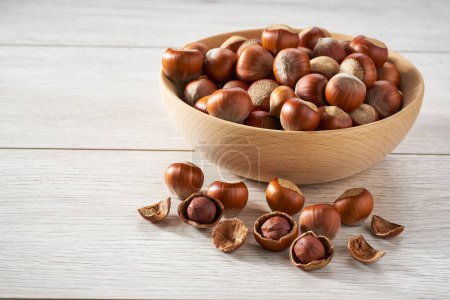 Photo for Wooden plate with hazelnut nuts on white table. - Royalty Free Image