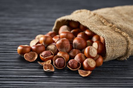 Foto de Hazelnut nuts in burlap sack on black wooden table. - Imagen libre de derechos